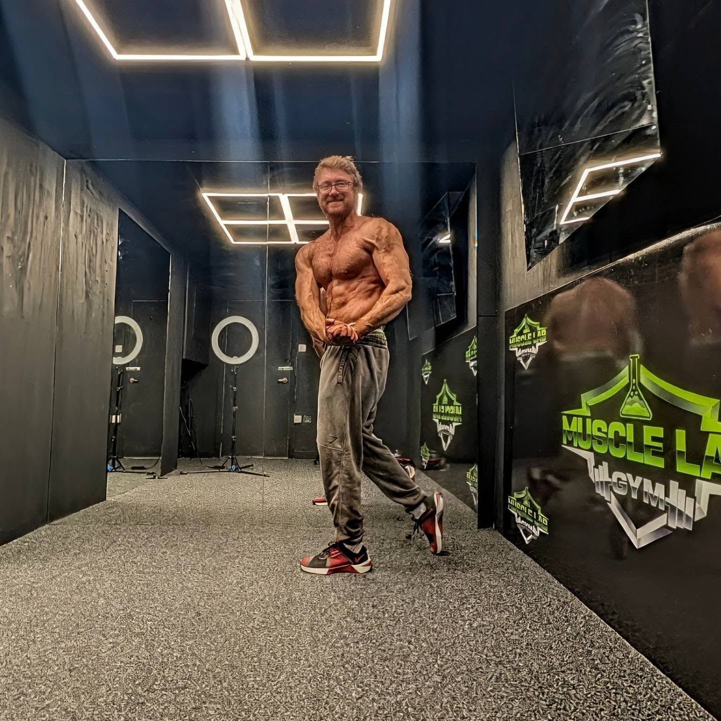 A Muscle Lab member posing under the gym's LED light rig, Muscle Lab logos on the wall